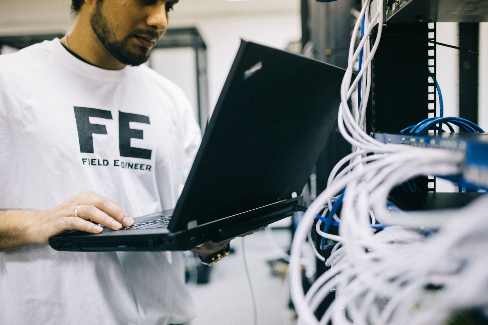 Ingeniero de redes trabajando en laptop junto a un rack de servidores